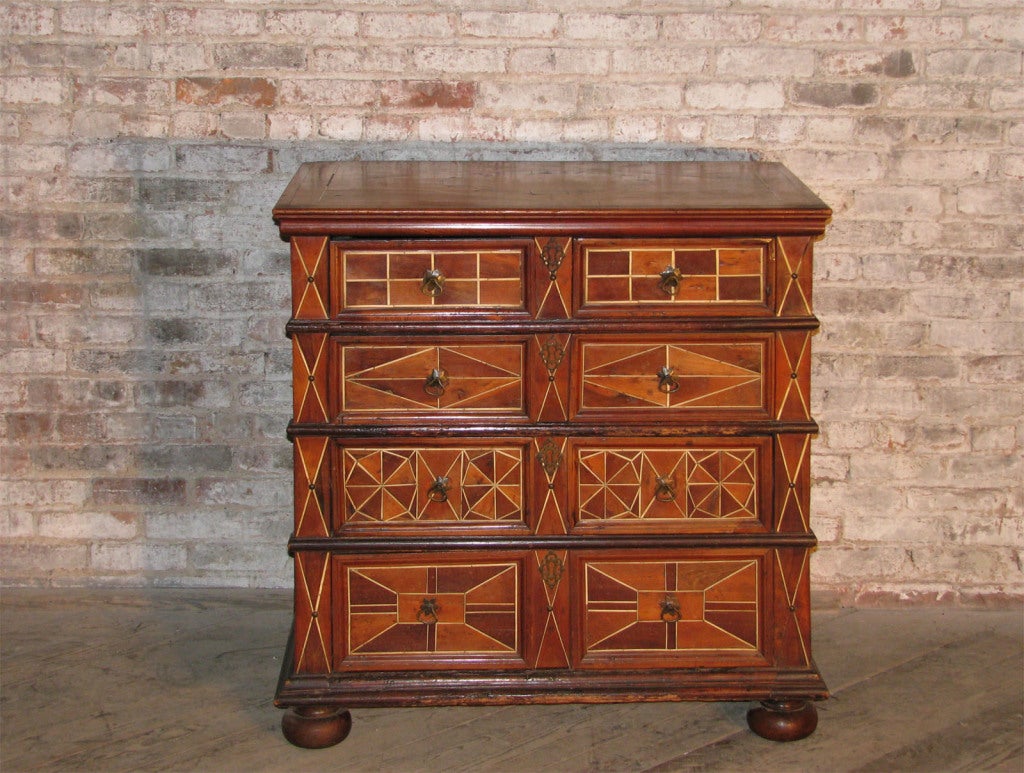 A strikingly decorative commode with fronts and top veneered with walnut and fruitwood, accentuated with bone stripes to form a vivid geometric design, paneled sides with strong wrought iron handles
Two small drawers over three large ones