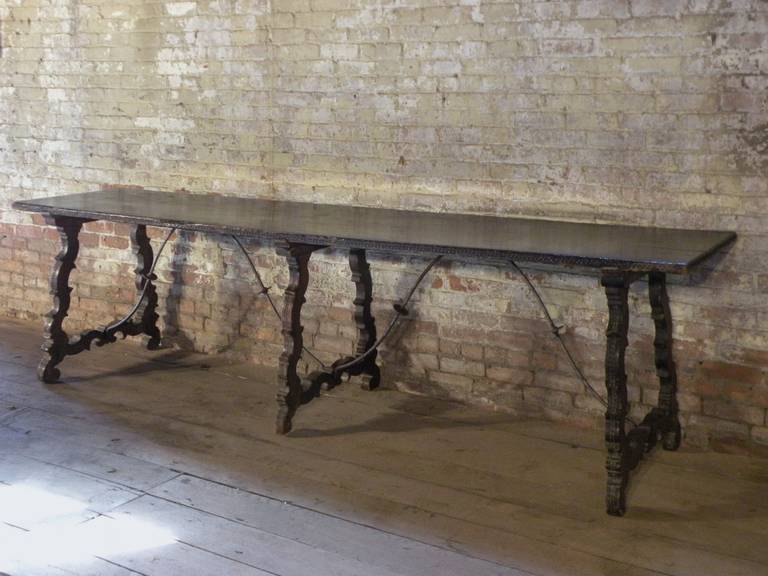 Long and narrow three-legged trestle table or console of rare proportions, with a one-plank top supported by three superbly shaped legs, joined by wrought iron stretchers.
The edge of the top and the outside of the legs showing a band of chip-carved
