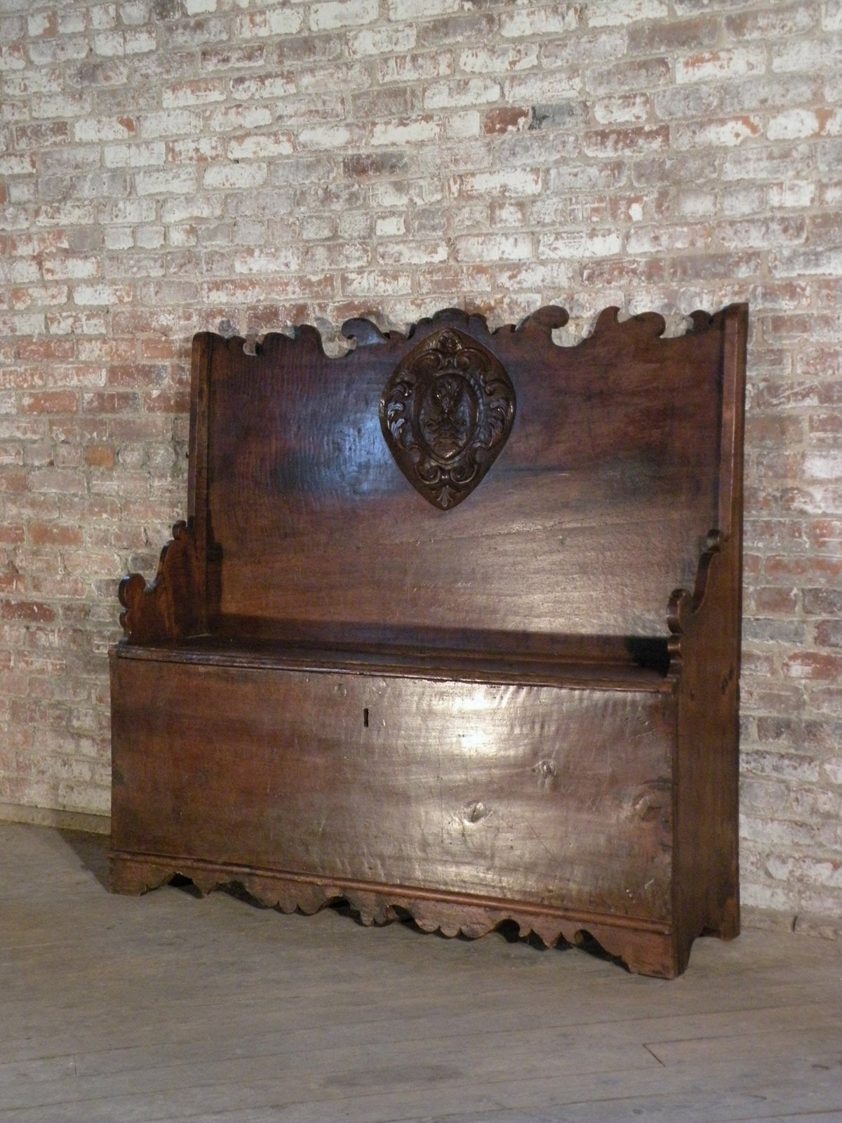 Attractive Italian cassapanca or hall bench, the unusually high back bearing a prominent carved crest in the center, the narrow seat having a lift top to reveal a storage compartment. Beautiful, rich patina.
Our pieces are left in lived-in