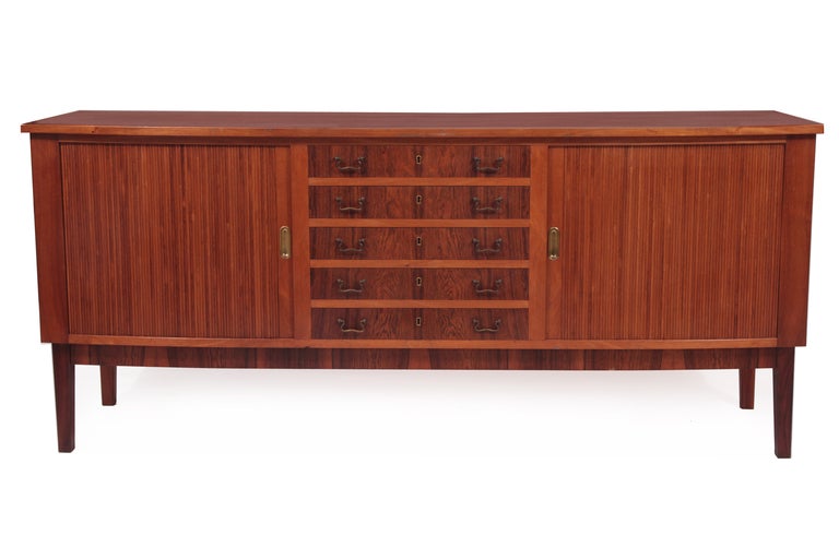 Beautiful rosewood and brass credenza or chest of drawers from Denmark, circa mid-1960s. This all original example has two rosewood tambour doors with inset brass pulls. Each side has an interior adjustable shelf and there are four centre drawers