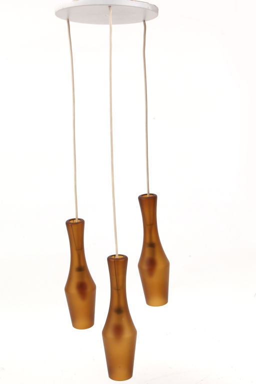 Amber glass and steel chandelier from Denmark, circa late 1960s. This example has three handblown amber glass cylindrical forms that unite with a steel top plate. This could be made into three pendants or sold as a chandelier. The height is