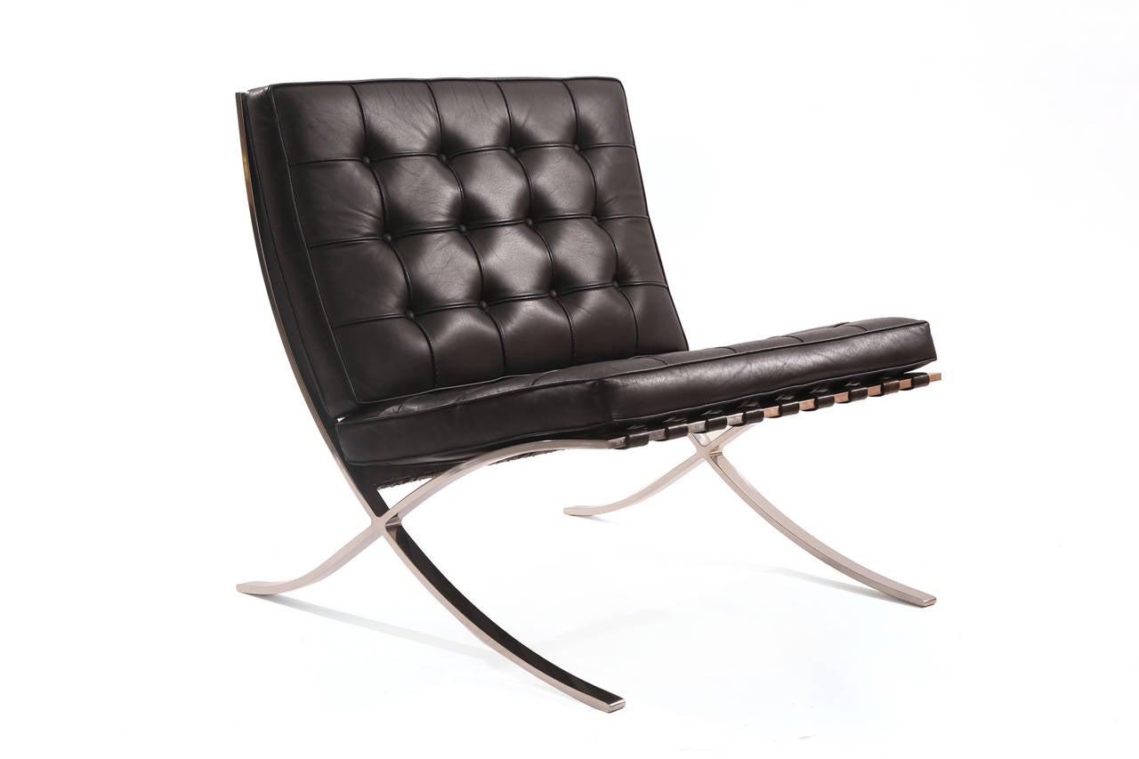 Early pair of Knoll Barcelona chairs and ottoman, circa early 1960s. These examples are stainless steel and are upholstered in a supple beautifully broken in black leather. Price listed is for the pair of chairs and ottoman.