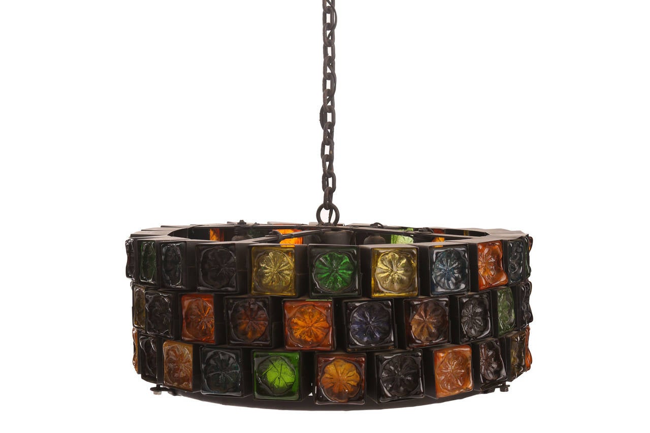 Stunning hand blown glass and wrought iron chandelier from Mexico circa early 1960's. This example has striking inset embossed glass with hues of reds oranges blues and greens in a black iron frame.