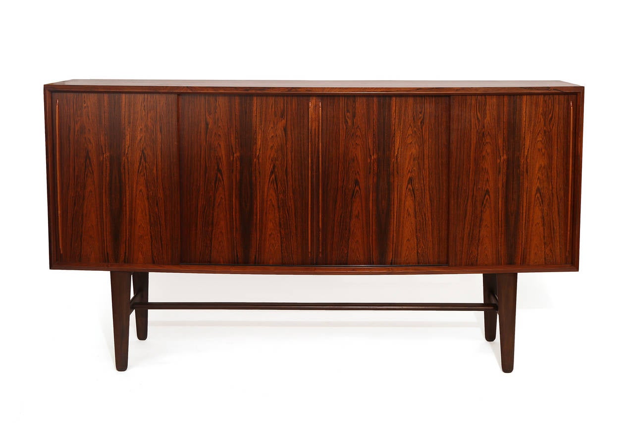 Fabulous rosewood sideboard or credenza by Dansk Designs, circa early 1960s. This all original example has incredible graining to the rosewood case, four tapered interior drawers and adjustable interior shelves. Excellent original condition.