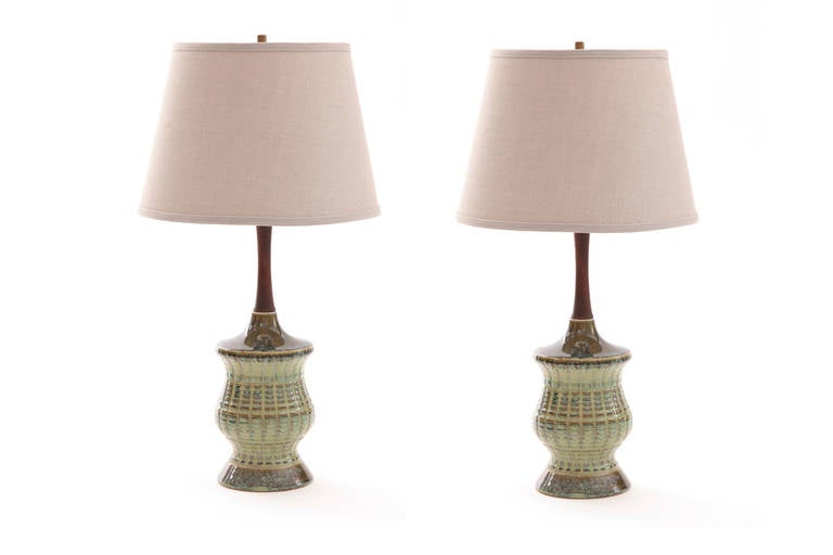 Pair of glazed ceramic and walnut table lamps, circa late 1950s. These lovely examples have hues of greens and earth tones with tapered walnut accents. Price listed is for the pair. Shade measures at height 10