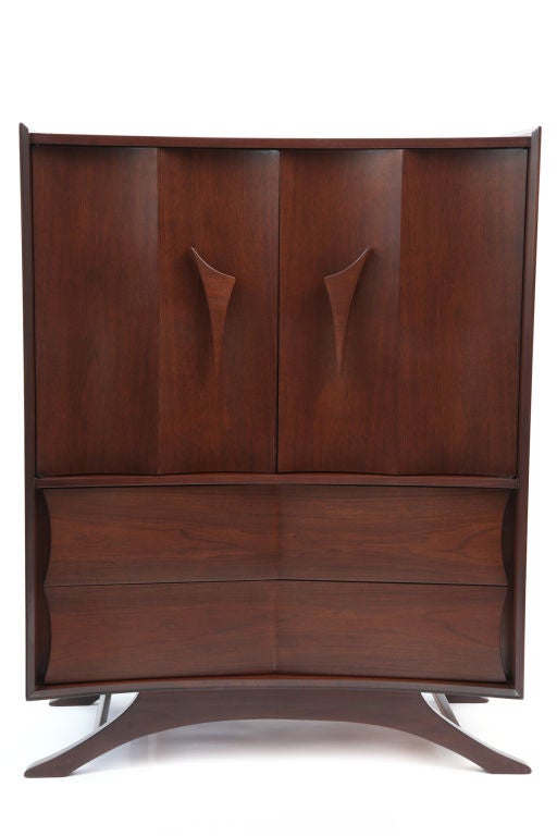 Phenomenal walnut highboy circa early 1960's. This subtly curved example has large free form door pulls 6 drawers for more than ample storage  wonderful curved doors and sculptural splayed legs. Please see our other listings for the matching chest