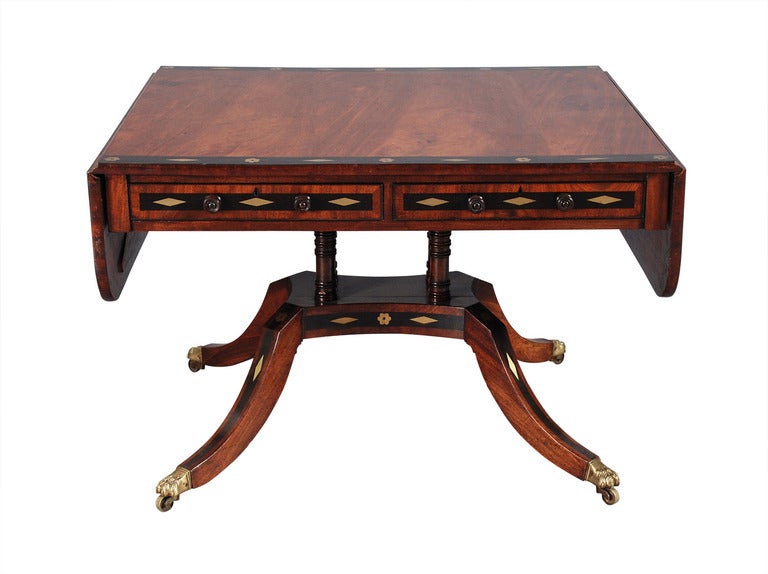 A Regency period mahogany library table with ebonized cross-banding inlaid with brass diamonds and rosettes. Great figuring to the timber. Lovely color. Two drawers on one side, two dummy drawers on the other. In the manner of George Bullock. 42.5
