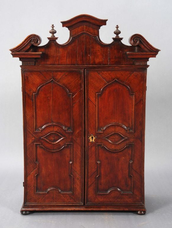 An Italian wall cabinet, 18th century with an architectural cornice over a pair of arched panelled doors enclosing shelves, now on low bun feet