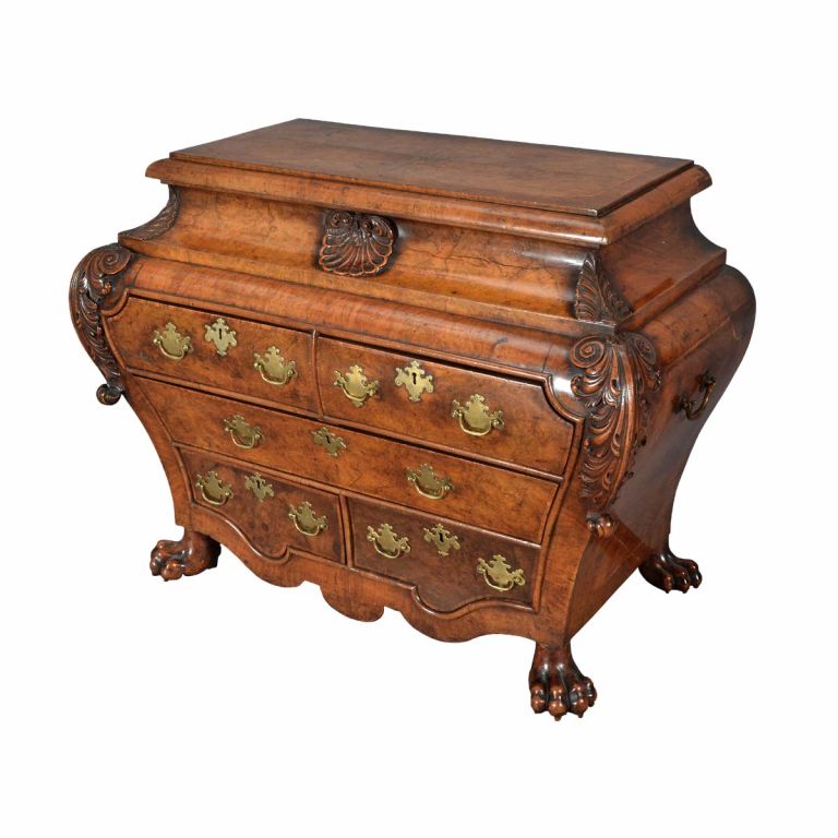 All of the crisply carved elements (the feet, acanthus leaf corners, and center shell) are executed in boxwood. The quarter-veneered and hinged top is outlined by cross-banding which in turn surrounds an inlaid band of boxwood. While the bombé shape