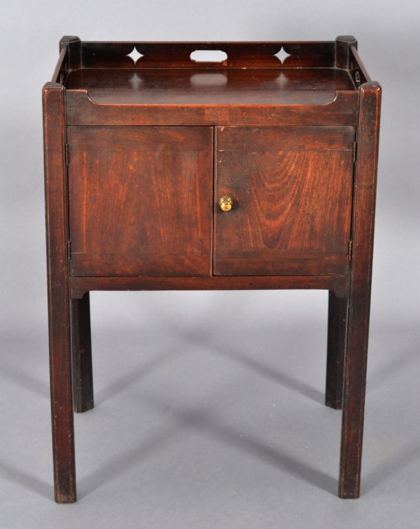 An English mahogany bedside cupboard with two doors beneath a gallery pierced with diamonds and handholds. Raised on straight molded legs.