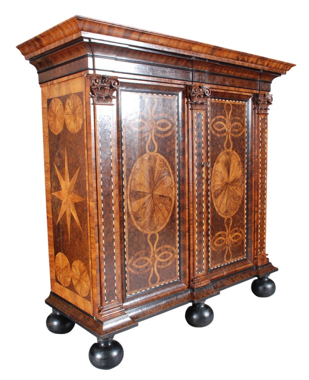 An oyster-veneered kas on the original ebony bun feet. The pilasters on the doors with ebony and ivory checkered inlay and topped with crisply carved Corinthian capitals. The geometric patterns of the front and sides outlined with ebony line inlay.