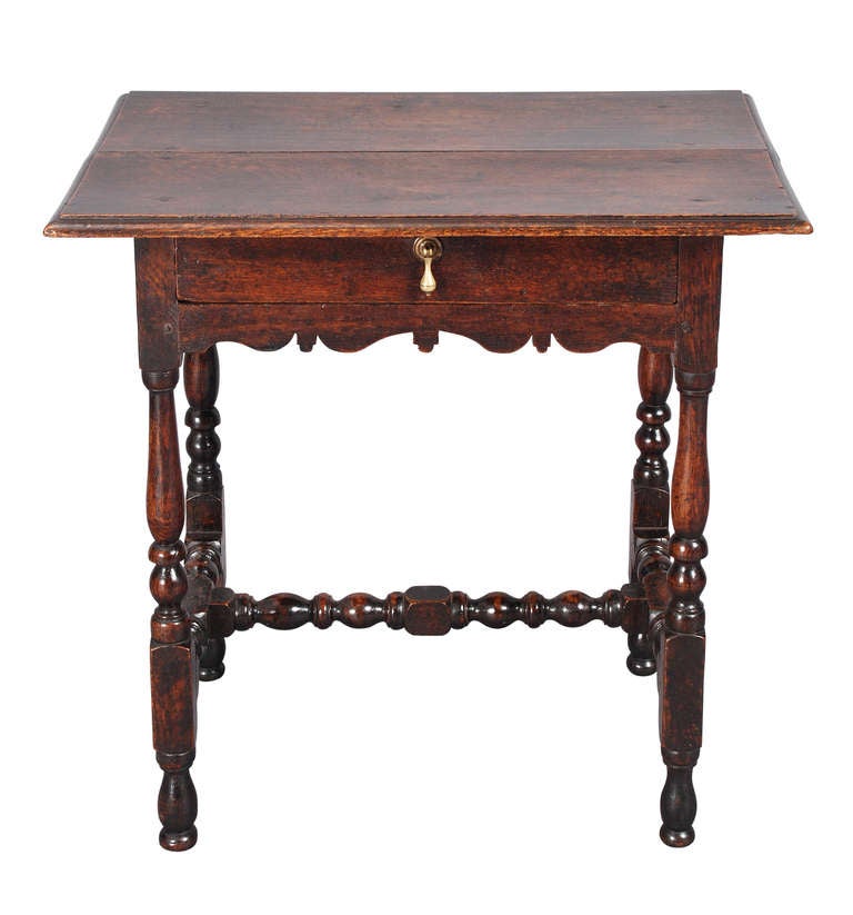 An oak side table on turned legs connected by high, H-stretchers. With a shaped apron below the frieze drawer. The molded edge top has a nice overhang. Retaining a good, rich color and patina.