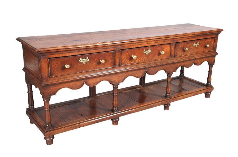 An oak dresser on substantial, baluster-turned legs connected by a potboard below and raised on turned feet. The three cock-beaded drawers with brass knob handles. The shaped apron also outlined with a cock-beading. Retaining a lovely, faded color.