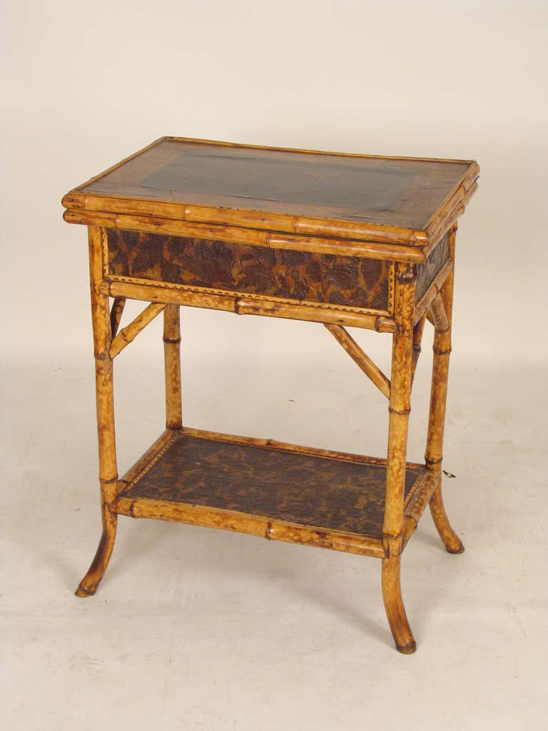 Bamboo games table with a chinoiserie decorated top and embossed paper mache frieze and bottom shelf, circa 1900. Please note the dimensions of the width and depth are measured at the feet. The width and depth of the top is, 25