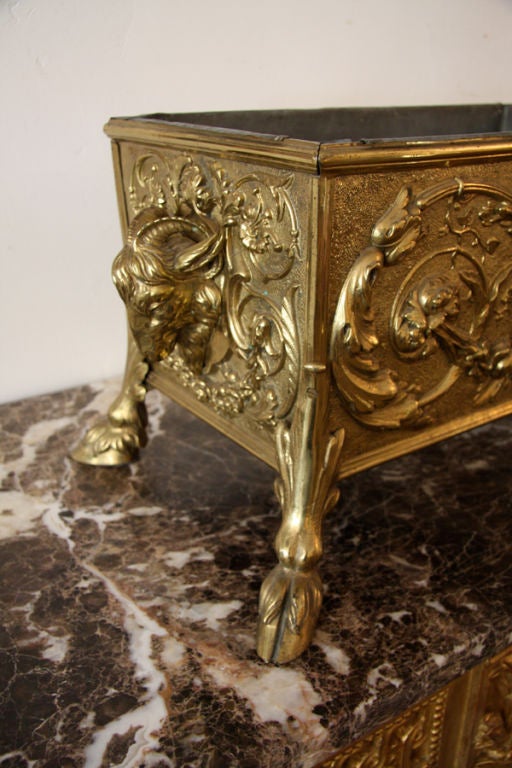 A brass repose French planter with ram head handles and hoof feet.