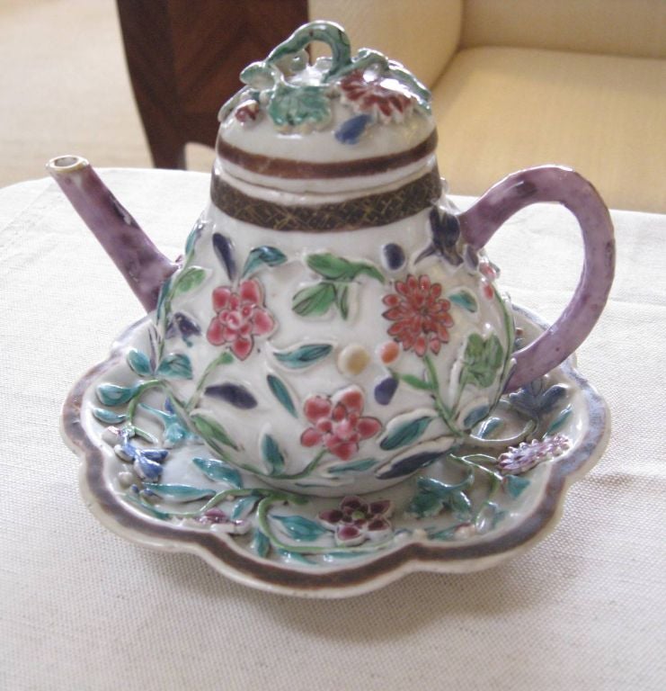 Early 19th Century famille rose teapot and saucer with applied floral decoration. There is an iron oxide border with detailed gold leaf geometric design in the borders of both. The saucer has a scalloped shape and a central lotus design surrounded
