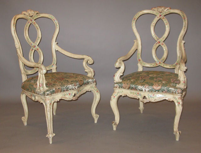 A pair of polychrome wood armchairs with moldings and painted floral decoration, each with a pierced cartouche shaped back with a carved shell above an interlaced splat, flanked by outscrolled arms and supported by cabriole legs ending in scrolled