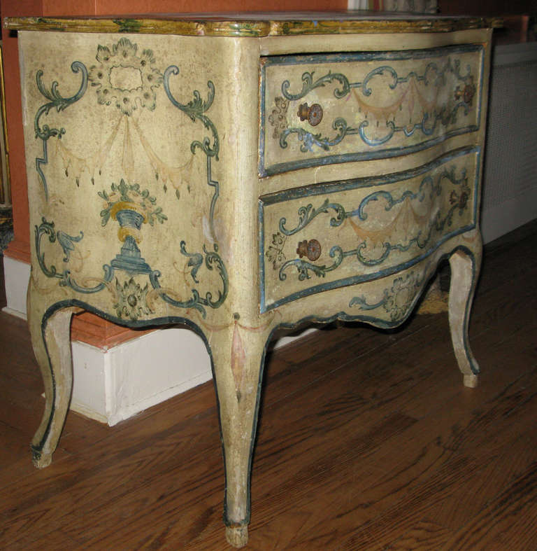 An Italian Rococo cream painted floral decorated commode with scalloped apron, cabriole legs ending in pied de biche feet; with a faux marbleized painted top.