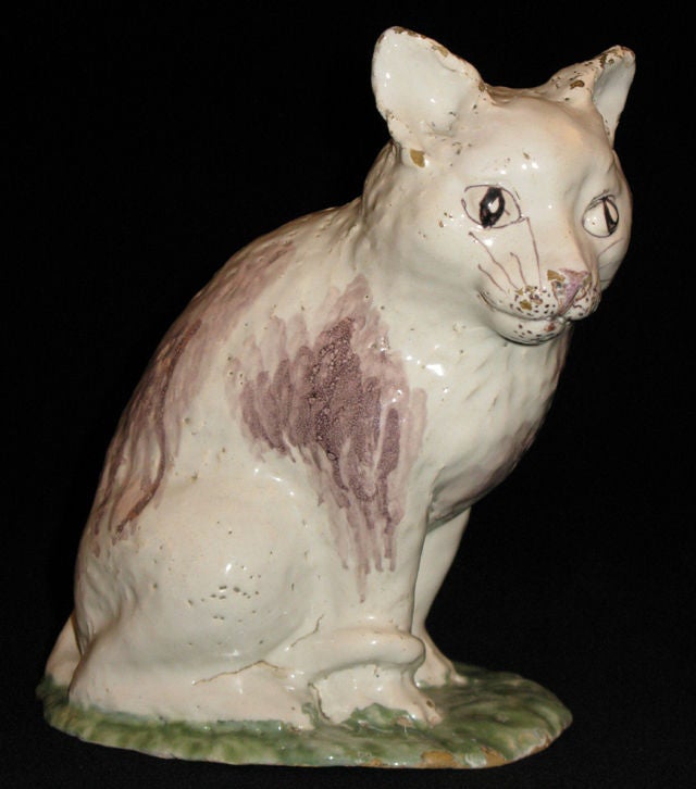 A faience model of a seated cat painted in green and manganese red.