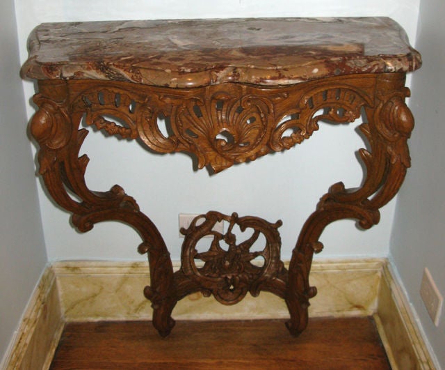 A fine ajouré (openwork) oak carved Regence/Louis XV console table with its molded and shaped Rouge Royale marble top.  The rocaille, shell, and foliate carvings are pierced in the apron, the legs, and the shell shaped design of the stretcher.