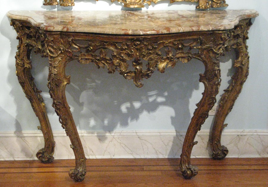 An Italian finely carved and mecca gilded console with a central espagnolette and a marble top; the cabriolet legs elaborately carved with leafs and vines, terminating in scrolled feet.