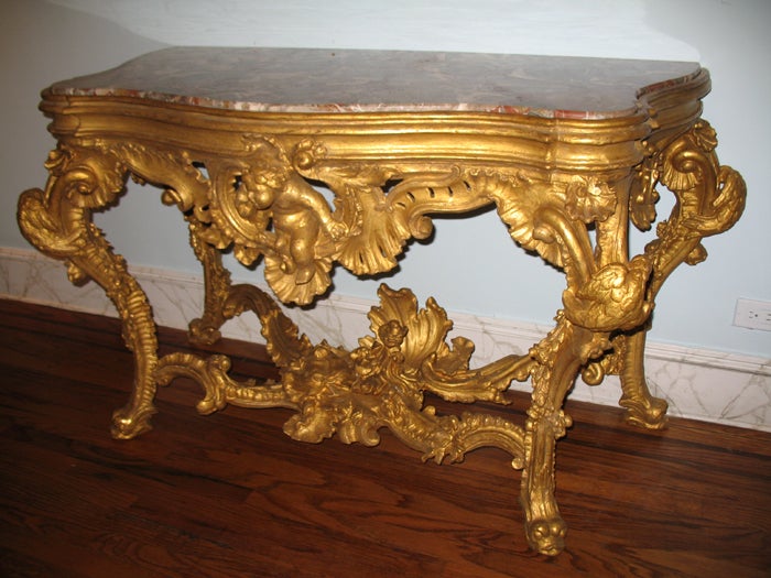 An elaborately carved and gilded console table with eagles clasped around the dental carved legs which have a shell at the top comprising two scrolls with open work and cascading flowers and garlands and terminating with dolphin feet.  The center