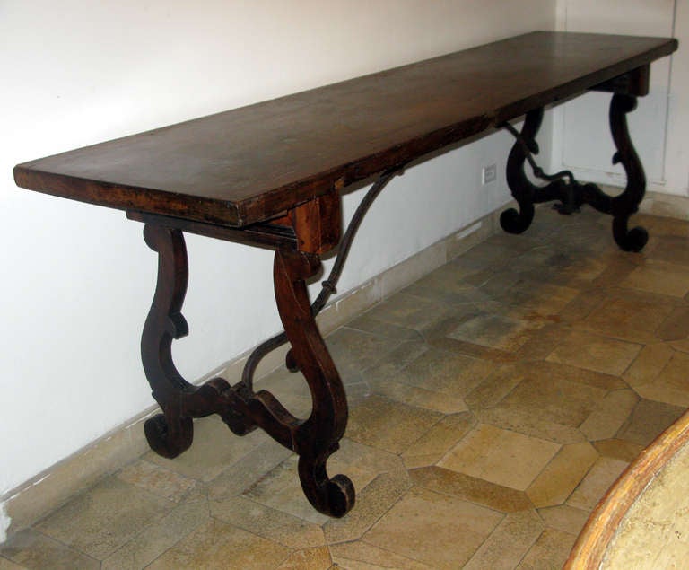 A walnut refectory table with lyre form leg supports and iron stretcher; the solid walnut top a single plank.