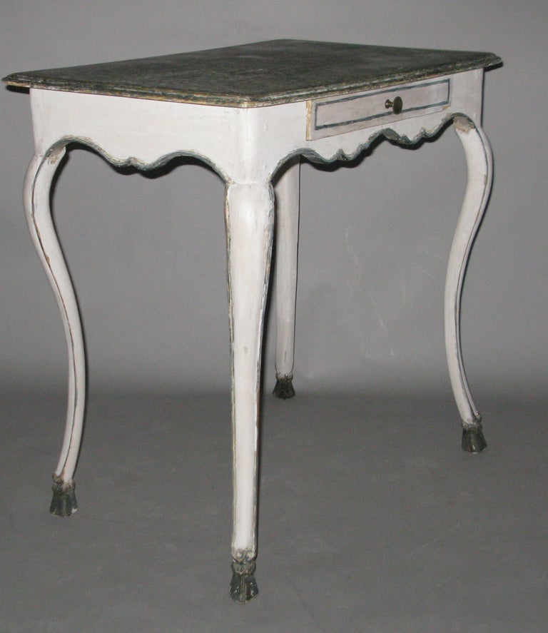 A single drawer painted white table with faux blue and green painted marble top, the shapely frieze decorated all around with blue trim; the cabriolet legs with blue trim and ending in pied de biche feet. 



