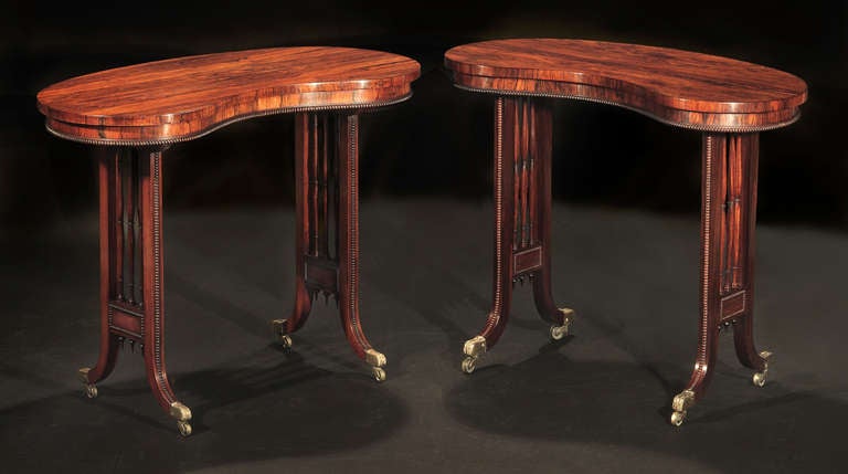 Each with shaped top over a beaded frieze, on standard dual-splayed end supports with turned spindles, raised on foliate brass caps and casters.