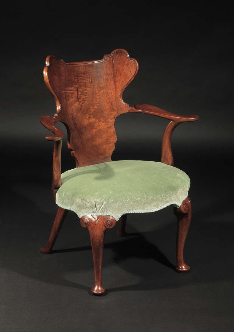 The solid backsplat constructed of finely figured timber of tapering form with molded edge, issuing boldly out swept arm rests on curved supports; the cabriole legs headed by carved scrollwork and ending in pad feet.