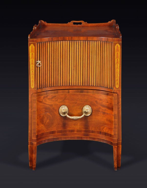 The concave-front rectangular top surmounted by a shaped gallery with pierced handles over a tambour door set between engraved pendant husk garlands, above a deep drawer; raised on square tapering legs.