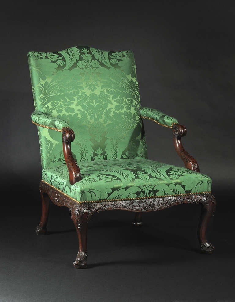 The rectangular padded back issuing straight padded armrests terminating in downward sloping foliate carved supports, above a padded seat raised on carved showwood frame with foliate carved cabriole legs ending in scroll form feet.