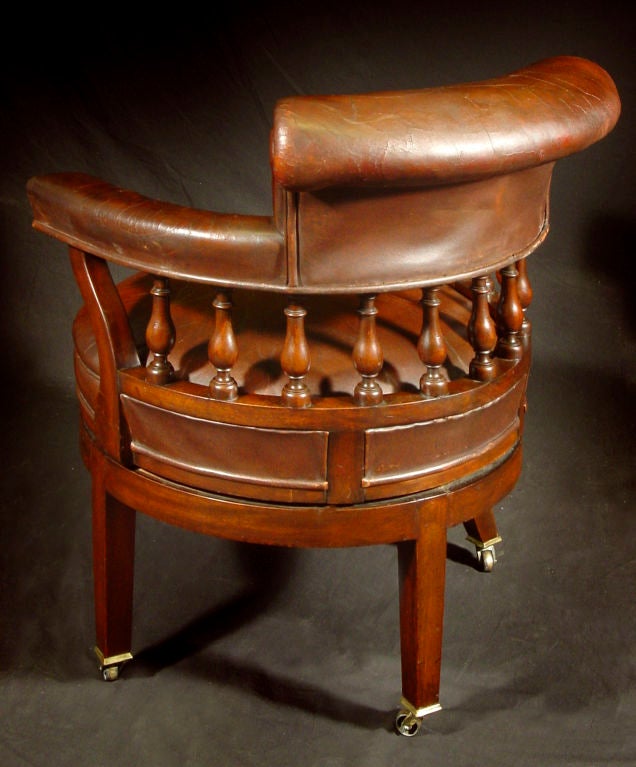 The leather-upholstered tablet-form back issuing padded armrests over baluster-form supports; the rounded swiveling seat over square tapering legs on casters.