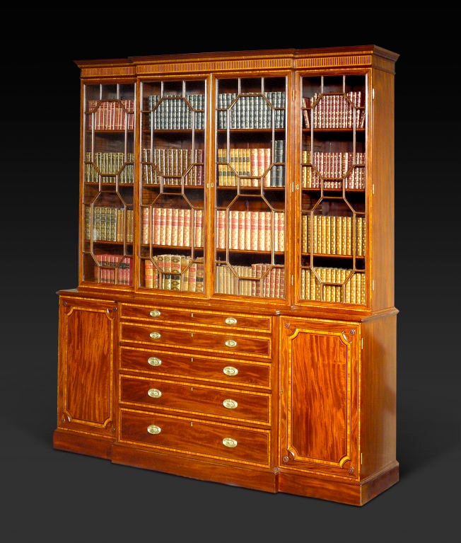 The dentillated cornice with blind stop-fluted frieze over four glazed doors with octagonal mullions opening to adjustable shelves; the lower part fitted with a secretaire drawer simulated as two-drawer fronts enclosing a leather-lined writing