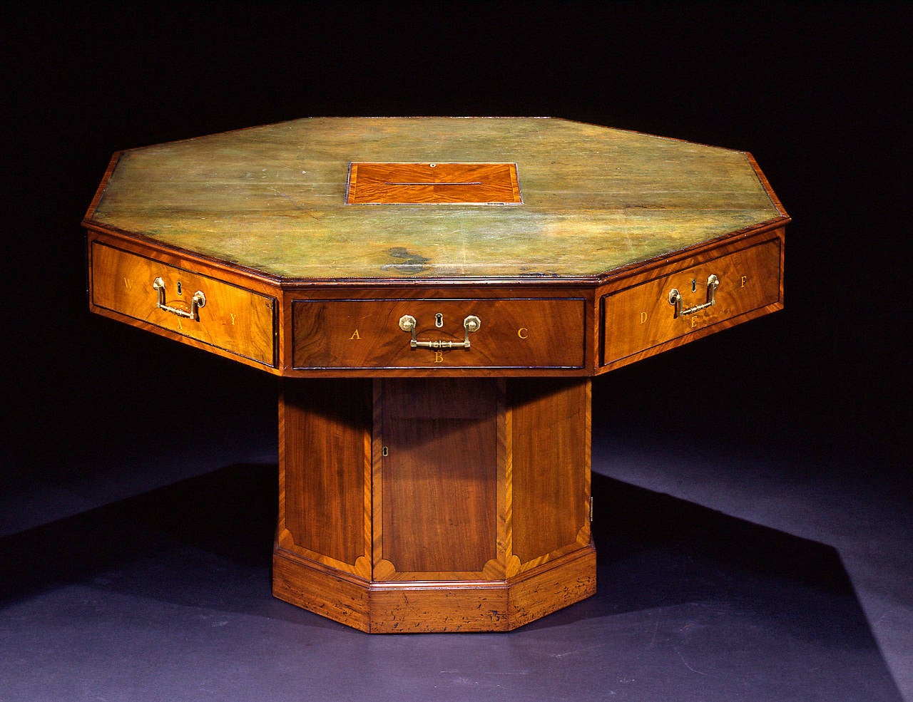 The revolving leather-lined top inset with a central hinged ratcheted letter slot, above eight frieze doors each inlaid with letters; the octagonal pedestal support with tulipwood crossbanding fitted with a cabinet door opening to a shelf; on a