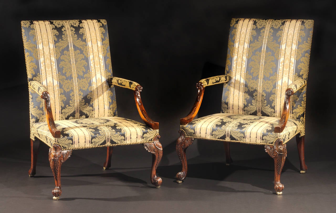 Each with rectangular upholstered back issuing padded armrests with foliate carved uprights terminating in flower-heads; raised on front cabriole legs finely carved with foliate sprays and terminating in scroll-form feet on casters; three legs