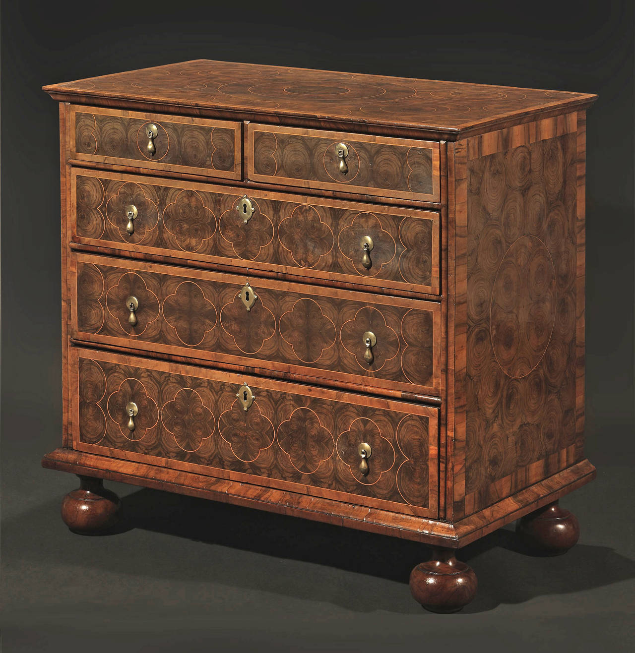 The rectangular top inlaid with sycamore concentric circular line inlay, over two short and three long graduated drawers, on bun feet; with walnut crossbanding throughout; replaced hardware.