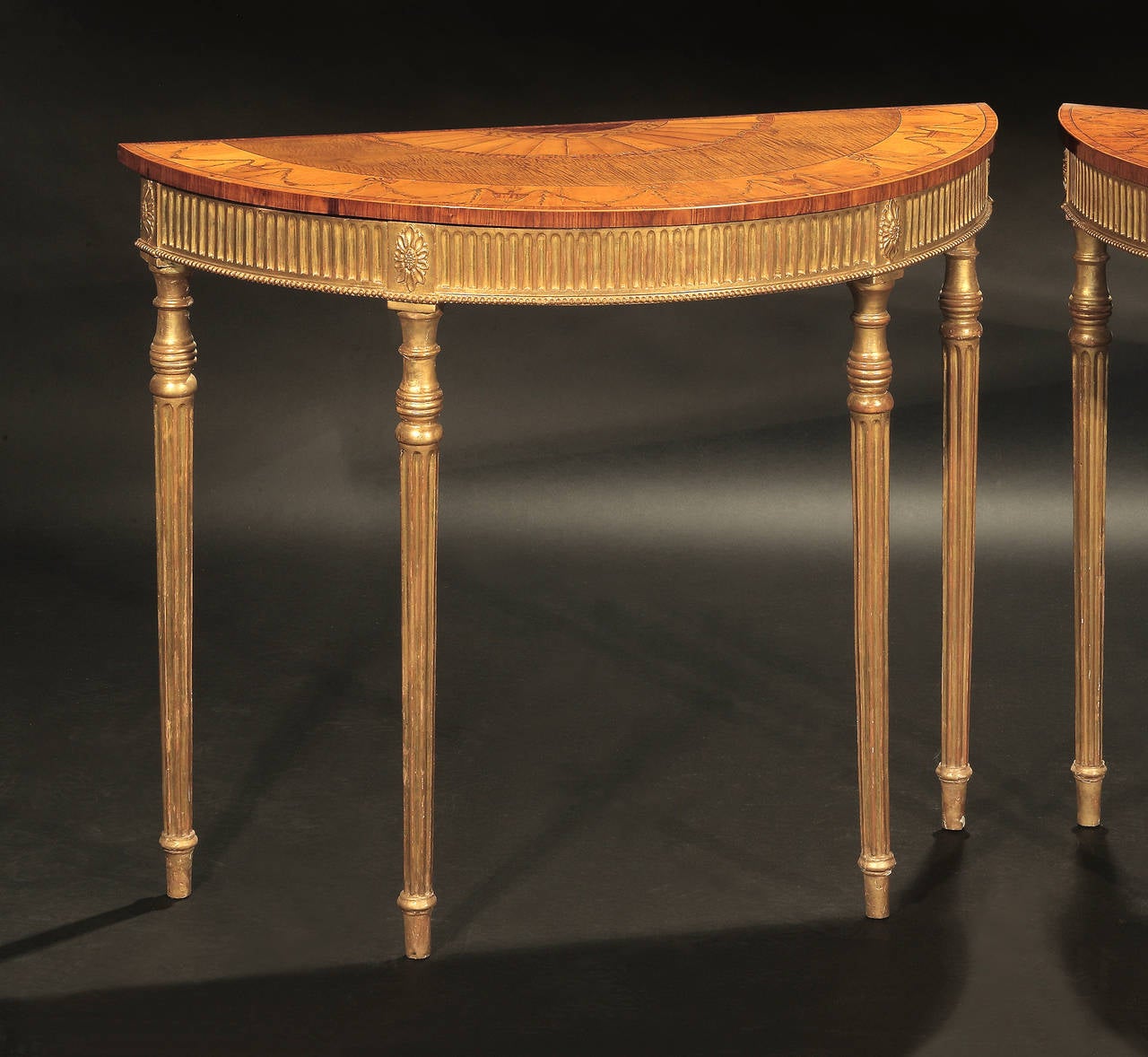 Fine pair of George III giltwood and each top inlaid with an elaborate fan paterae and broad satinwood border with ribbon-tied husk garland and Classical urn decoration, over a fluted frieze with beaded edge; raised on ring-turned fluted tapering