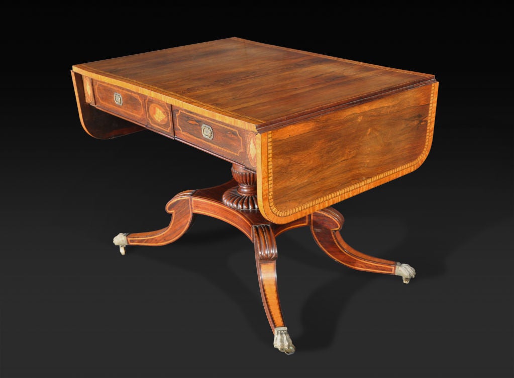 The rectangular top with D-shaped drop leaves with broad satinwood crossbanding and dentil inlay over a frieze fitted with two short drawers set between shell inlaid panels, opposed by two simulated drawer fronts; raised on a turned columnar support