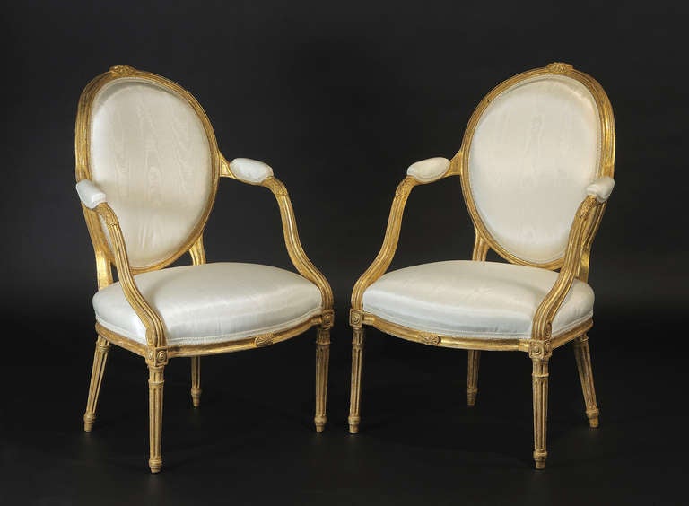 The padded backs set within a molded surround centered by a carved roundel; the padded armrests above acanthus carved and stop fluted down-swept supports terminating in a scrolled roundel; the molded seat rail of conforming serpentine form, raised