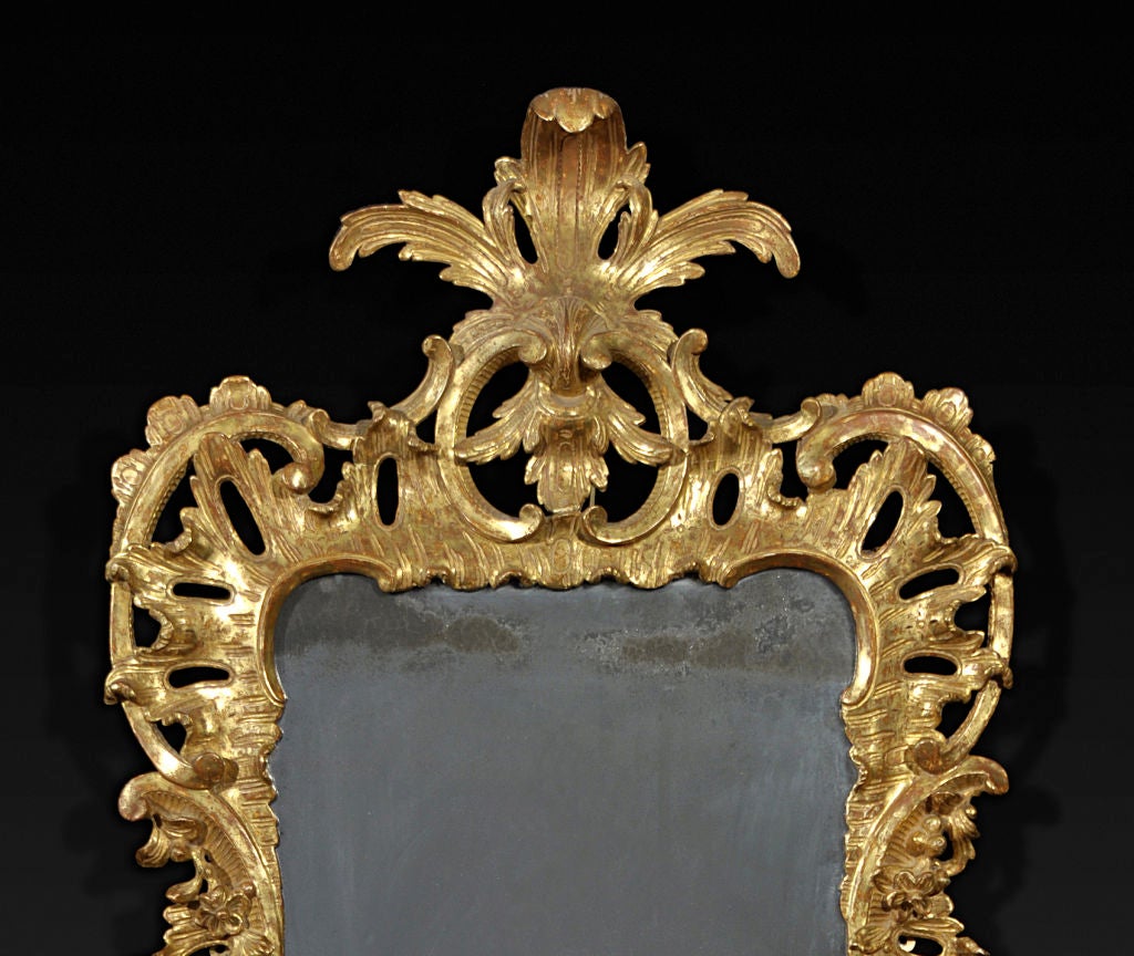 The rectangular plate enclosed by a surround exuberantly carved with C-scrolls, pierced cabochons and floral sprays and surmounted by a foliate clasp cresting.