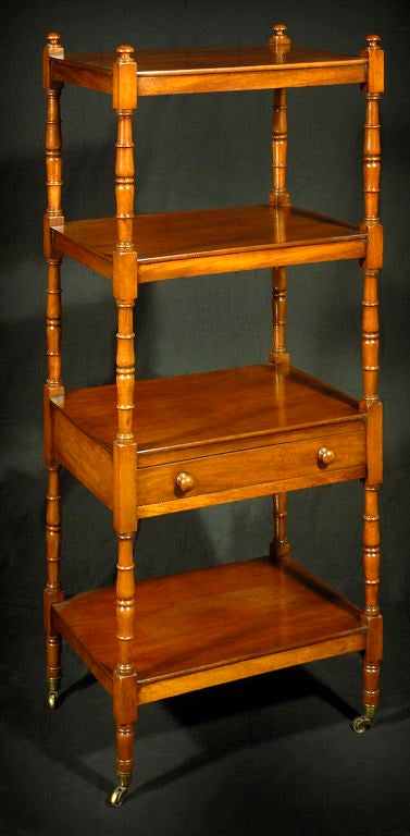 Mahogany four-tier étagère with one drawer; raised on turned, baluster-form supports on casters.