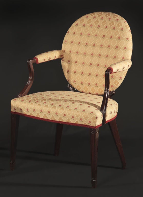 Oval upholstered back issuing shaped, out-stretched, and padded armrests above over upholstered seat, raised on square molded tapering legs.