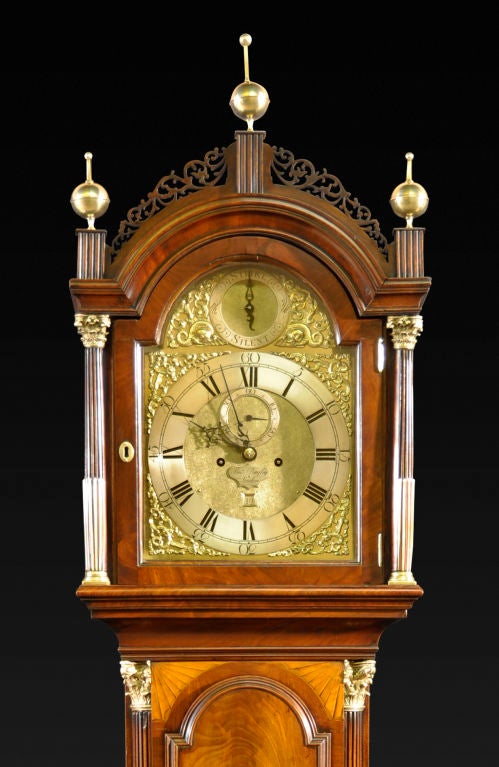 The arched hood surmounted by pierced scrollwork and ball finials over the brass dial with silvered chapter ring, seconds dial, calendar aperture set below the strike/silent dial, all enclosed by arabesque spandrels and flanked by brass-inlaid