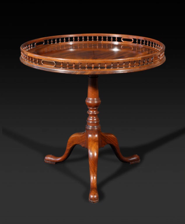The circular top with brass-strung balustraded gallery raised on a reeded columnar support issuing three acanthus and cabochon carved downswept legs ending in ball and claw feet.