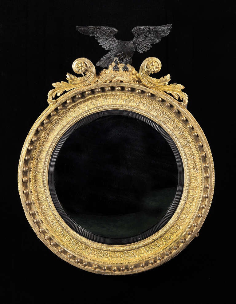 The circular mirror plate within an ebonised receded slip and conforming frame finely carved with foliate decoration and applied with spherules; surmounted by an outstretched eagle perched on a bed of rocks flanked by foliate scrolls terminating in