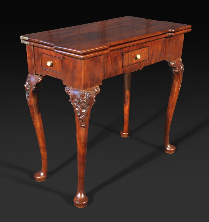 The rectangular top with outset corners opening to a leather-lined surface over a frieze fitted with a cockbeaded drawer to the centre and to each side; raised on cabriole legs carved with foliate scrollwork and ending in pad feet.