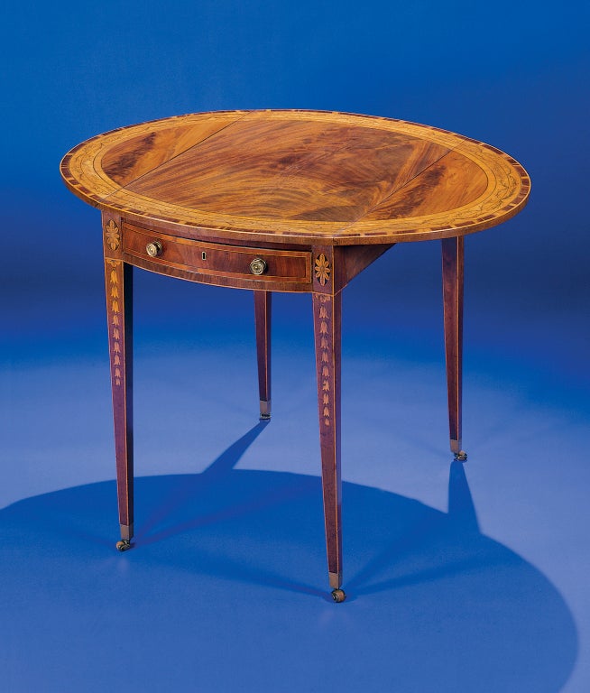 The highly-figured top with vibrant tulip wood and satinwood banding; the single frieze drawer flanked by floral roundels; raised on square tapering legs inlaid with bellflower swags.