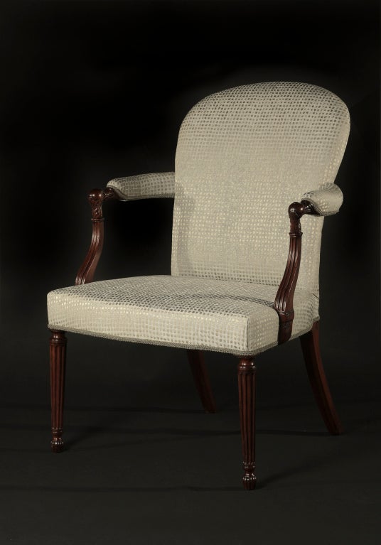 The upholstered back and seat flanked by padded armrests with foliate carved terminals; on round reeded tapering legs.