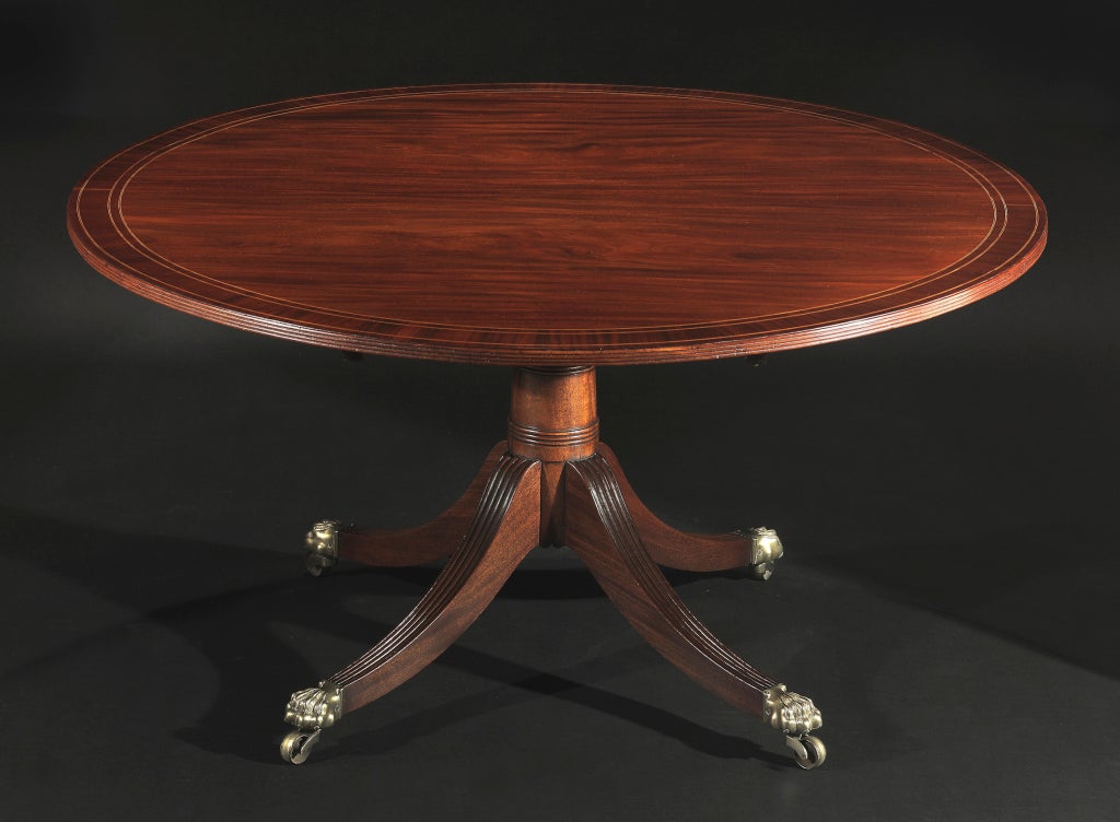 The crossbanded top with boxwood stringing and reeded edge, above a ring turned columnar support issuing four reeded downswept legs ending in brass paw caps and castors.